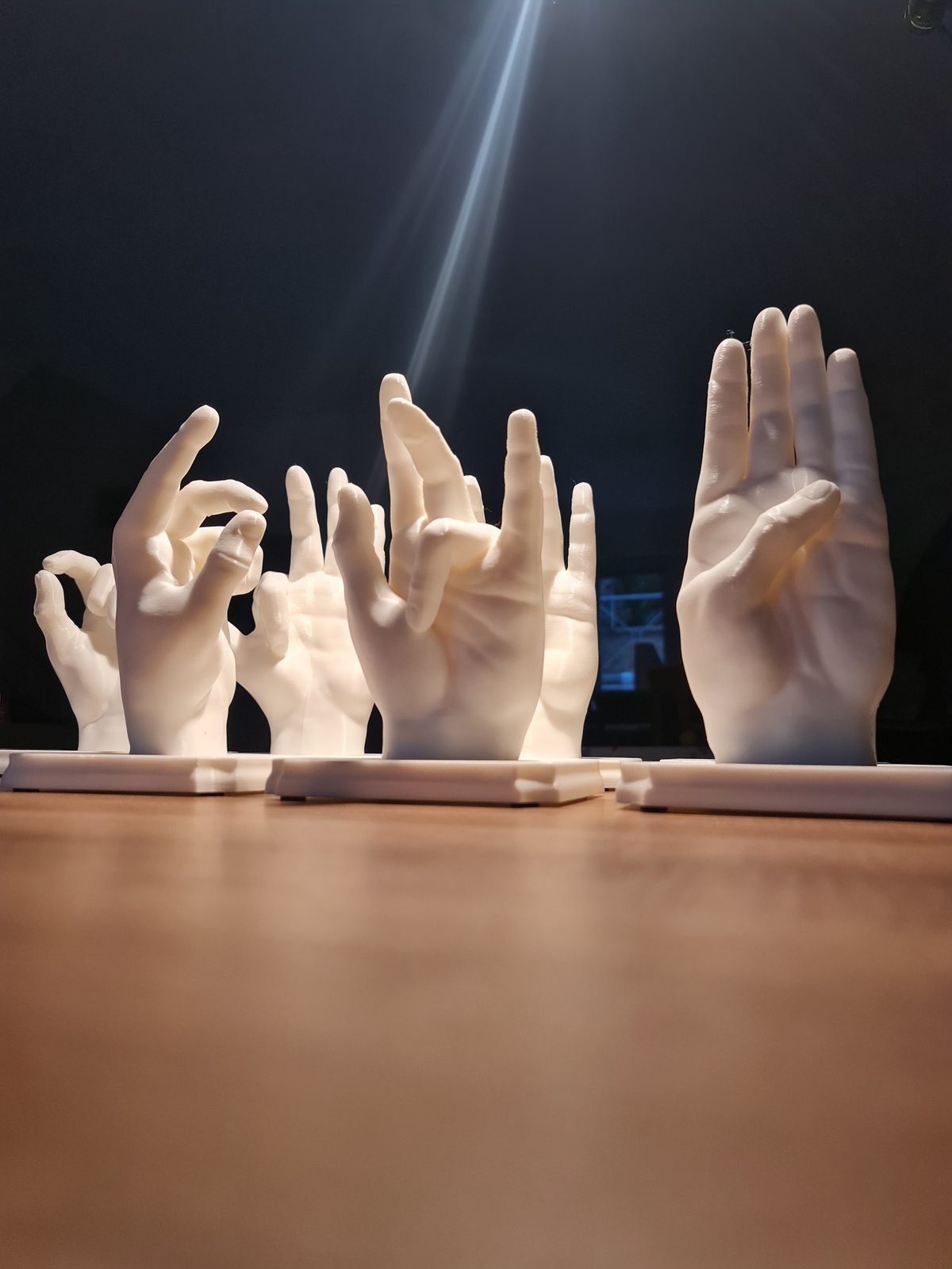 White 3D-printed hands in different gestures on their bases, lit from above by a beam of light